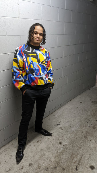 In this image Feng wears the Tidal Jumper with skinny jeans and shiney black leather shoes. His hands are in his pockets and he is looking straight at the camera with a suave smile. His black curly hair completes the look, the black jeans also complimenting the graphic elements of the jumper.