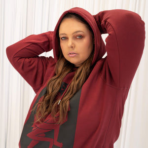 Krissy wears a Two Spirits Genderless Hoodie in rich Burgandy with the black Two Spirits print on the front and arms.