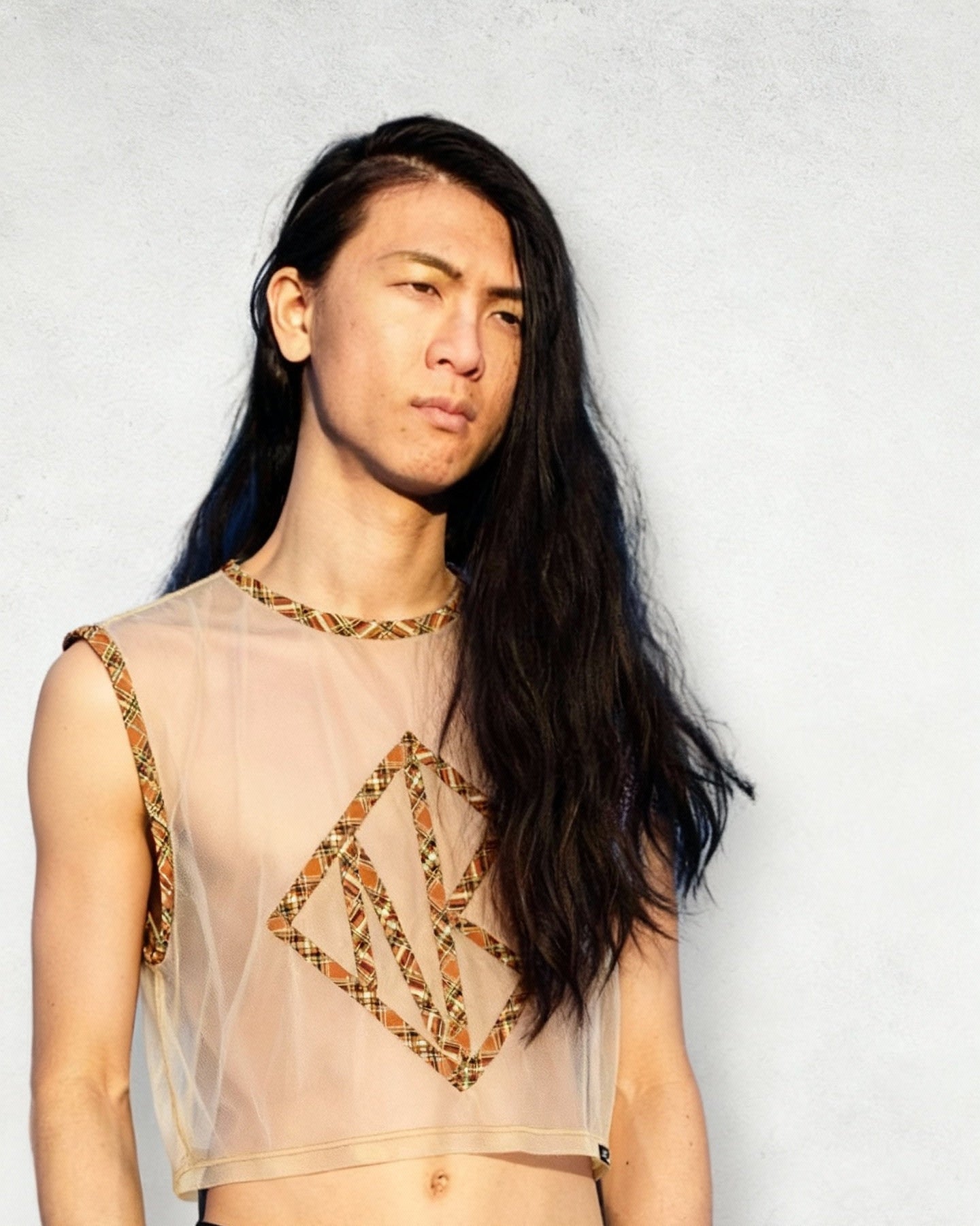 Person wearing a sheer top with geometric patterns hand sewn onto the front, standing against a plain background