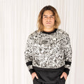 Sam wears the GNKY Jumper and GNKY Track Pants, he's looking straight at the camera and is standing face on with his hands in his pants pockets. The jumper is printed in black and white graphic style, with black cuffs at the wrist and bands half way between the wrist and elbow, as well as a black collar trim and hem band. The jumper has long sleeves and is a cropped length sitting just above high hip on a tall human like Same who is 195cm tall, or at the hips on a shorter human.
