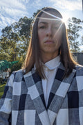 Person wearing a checked linen blazer with white crisp shirt underneath. The image is a close up showing the detail of the wide lapels, and there are trees and sunlight in the background