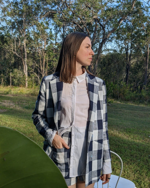 Model standing outdoors in a well made checkered linen jacket, a crisp white collared shirt underneath in front of a verdant natural backdrop.