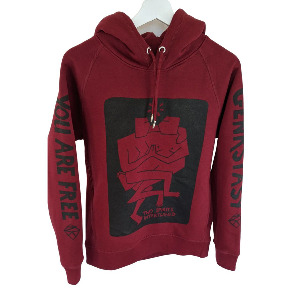 Details of rich burgandy red hooded jumper. Two hip pockets. Smooth metal finished hood loop and cord ends. On the front of the jumper is a black graphic art print of two figures intertwined together. It reads 'Two Spirits Intertwined. On the sleeves it reads 'You Are Free' on one and 'Genkskstasy' on the other'.