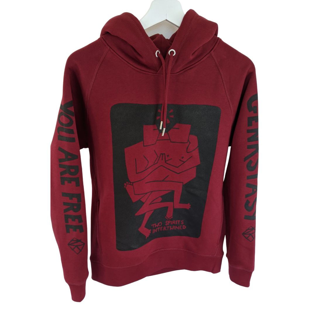 Details of rich burgandy red hooded jumper. Two hip pockets. Smooth metal finished hood loop and cord ends. On the front of the jumper is a black graphic art print of two figures intertwined together. It reads 'Two Spirits Intertwined. On the sleeves it reads 'You Are Free' on one and 'Genkskstasy' on the other'.