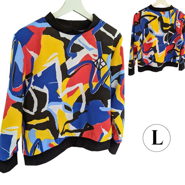 Size L Tidal Jumper, a fleecey full length sleeved, jumper which is a slightly boxy fit, and is cropped at the hip for ease of wearing in a wheelchair, or showing off your booty. The cuffs, collar and hem of the jumper are black cotton in contrast with the geometric colourful pattern of the main part of the jumper. The colours in the pattern are red, blue, yellow, white black, and pale blue. The shapes of the pattern are orgnaic but angular, a 1980s feel.