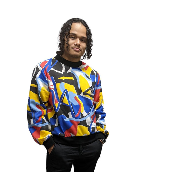 In this image Feng wears the Tidal Jumper which is a fleecey full length sleeved, jumper which is a slightly boxy fit, and is cropped at the hip for ease of wearing in a wheelchair, or showing off your booty. The cuffs, collar and hem of the jumper are black cotton in contrast with the geometric colourful pattern of the main part of the jumper. The colours in the pattern are red, blue, yellow, white black, and pale blue. The shapes of the pattern are orgnaic but angular, a 1980s feel.
